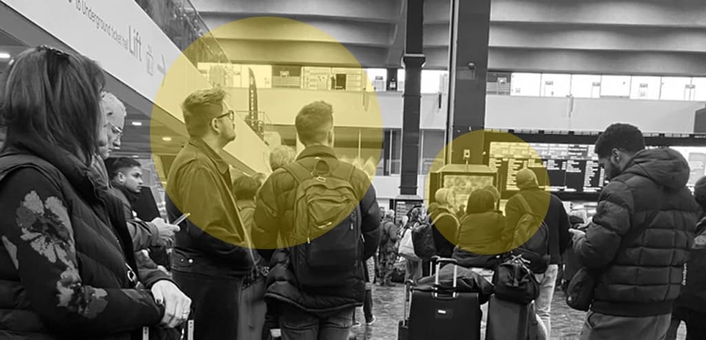 Passengers standing in a cluster beneath the departure boards while waiting.